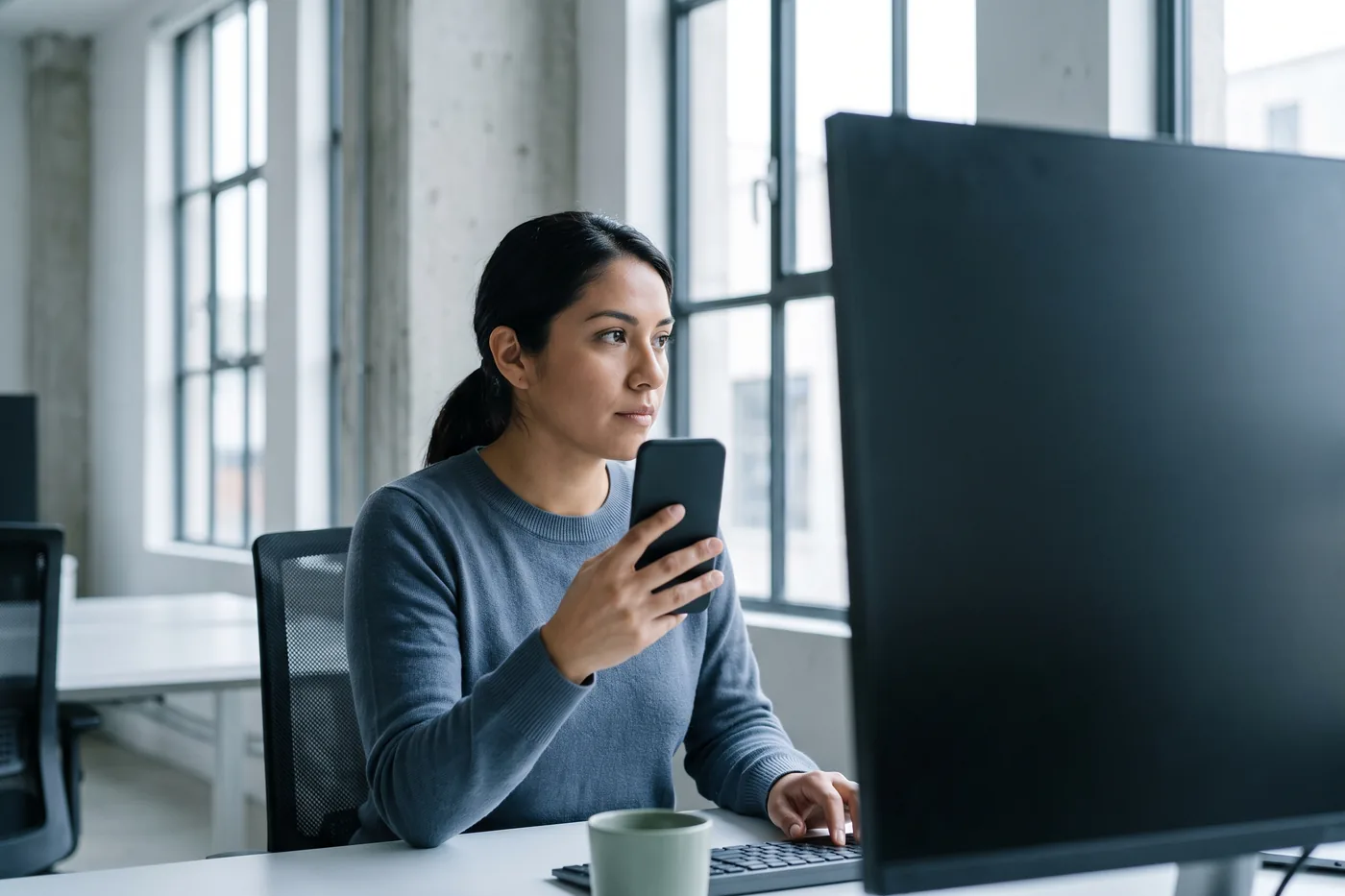 A product marketer checking a live website on her phone at her desk